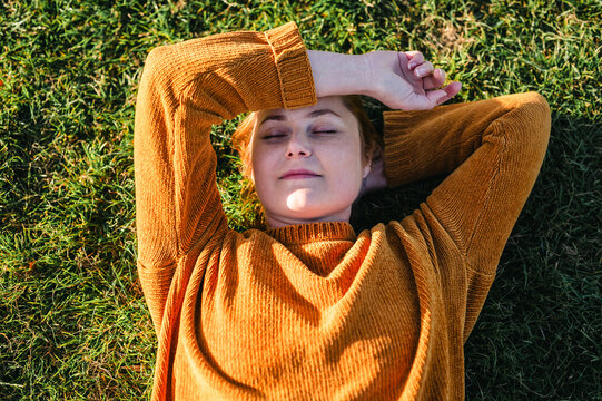 Woman relaxing with eyes closed lying on grass in warm sunlight