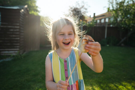 Happy child holding toasted marshmallow in sunny backyard garden