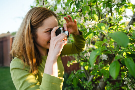 Young woman using vintage camera in blooming garden at sunset