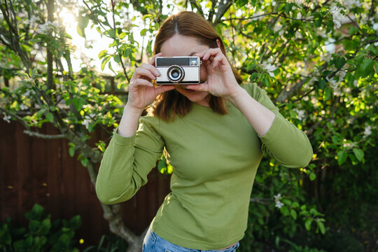 Young woman using vintage camera in blooming garden at sunset