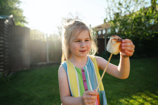 Happy child holding toasted marshmallow in sunny backyard garden