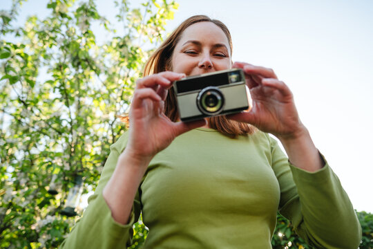 Woman photographing from low angle in sunny garden