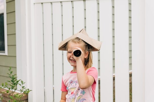 Young girl playing in backyard with paper hat and paper towel roll