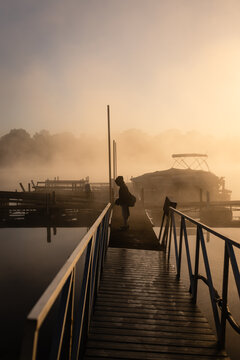 Boy fishing off dock at dawn on foggy lake