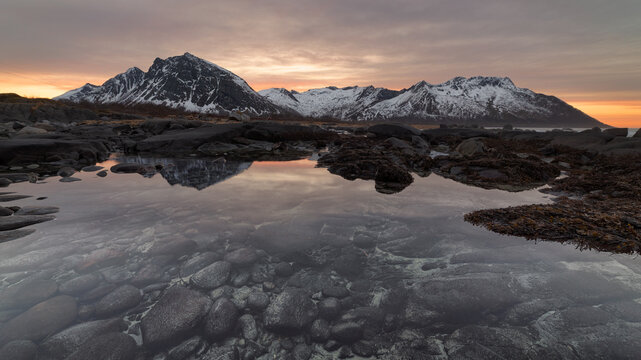 Rocky Coast Tide Pool Reflection at Sunrise with Snowy Mountains