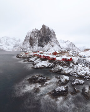 Snowy Coastal Village with Red Cabins and Mountain Backdrop