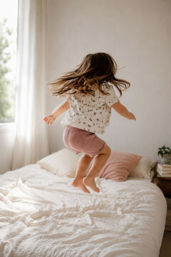 Energetic little girl jumping on bed in playful childhood moment