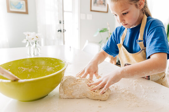 Child kneads dough while making bread in bright kitchen