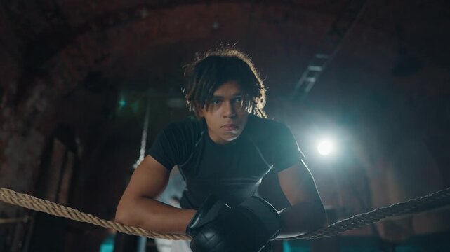 Young african american sportsman resting after box fight on ring, portrait shot. Exhausted professional fighter breathing hard, thinking about tactics of fighting, energy and power of combat sports