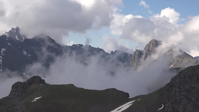 Timelapse clouds pass cliff slope, Jammu Kashmir Himalayas, landslide scar, snow patches. Accelerated sky motion crosses jagged precipice flank karakoram realm failed sediment apron thaw traces.