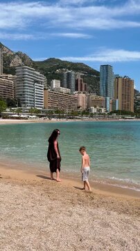 Attractive woman in dress and with her son walking on the beach in Monaco, Monte Carlo