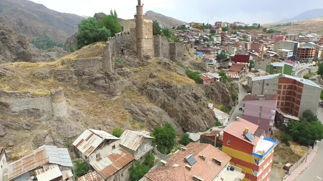 Aerial ancient hilltop fortress overlooking dense town houses in rugged valley under soft daylight. Birds eye shot stone castle tower crumbling ramparts and crowded rooftops beside river.