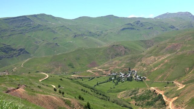 Panoramic Eastern Anatolia Turkey village, mosque, treeless green mountains, winding roads. Wide highland hamlet minaret bare slopes summer pasture remote countryside landscape.