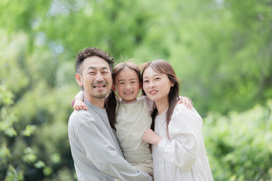 A close-up of a happy family of three smiling together amidst the fresh greenery, capturing their bond and happiness as they look directly at the camera