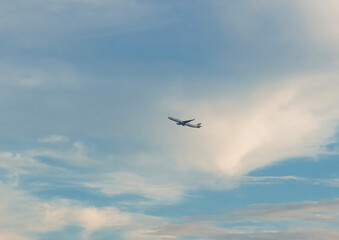 Fototapeta premium An commercial airplane flying high in the blue sky among soft white clouds during the day.