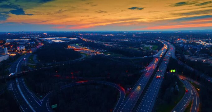 Vehicles with their headlights on move by the multiple highways in the huge interchange. Commuting in the city at sunset. Aerial view.