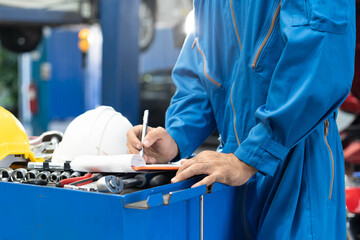Naklejka premium Auto check up and car service shop concept. Mechanic writing job checklist to clipboard to estimate repair quotation to client at workshop garage.