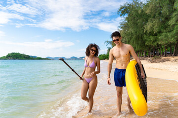 Obraz premium Loving couple carrying a paddleboard and walk along the sandy beach. 