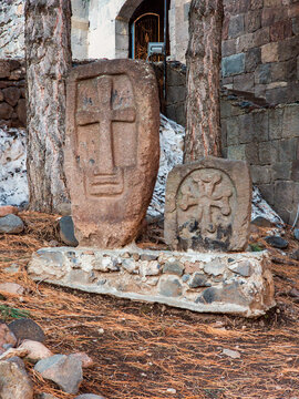 Weathered Armenian khachkars stand near ruined church structure with snow