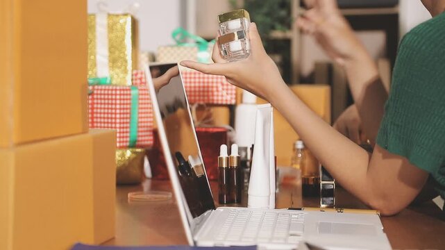 Young beautiful Asian girl reviewing cosmetic and skin care product with new collection's promotion selling on social media online live blurred phone screen surrounded beauty merchandise. Stratagem.