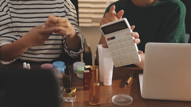 Young beautiful Asian girl reviewing cosmetic and skin care product with new collection's promotion selling on social media online live blurred phone screen surrounded beauty merchandise. Stratagem.