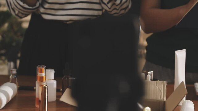 Young beautiful Asian girl reviewing cosmetic and skin care product with new collection's promotion selling on social media online live blurred phone screen surrounded beauty merchandise. Stratagem.