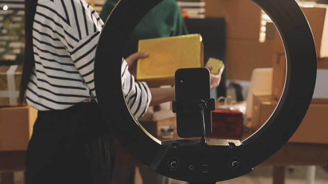 Young beautiful Asian girl reviewing cosmetic and skin care product with new collection's promotion selling on social media online live blurred phone screen surrounded beauty merchandise. Stratagem.