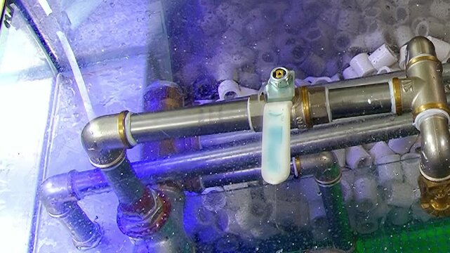 A vibrant blue light bathes the intricate metal pipes and active bubbles within a transparent tank.