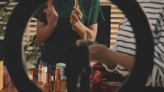 Young beautiful Asian girl reviewing cosmetic and skin care product with new collection's promotion selling on social media online live blurred phone screen surrounded beauty merchandise. Stratagem.