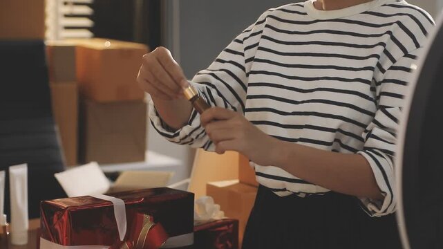 Young beautiful Asian girl reviewing cosmetic and skin care product with new collection's promotion selling on social media online live blurred phone screen surrounded beauty merchandise. Stratagem.