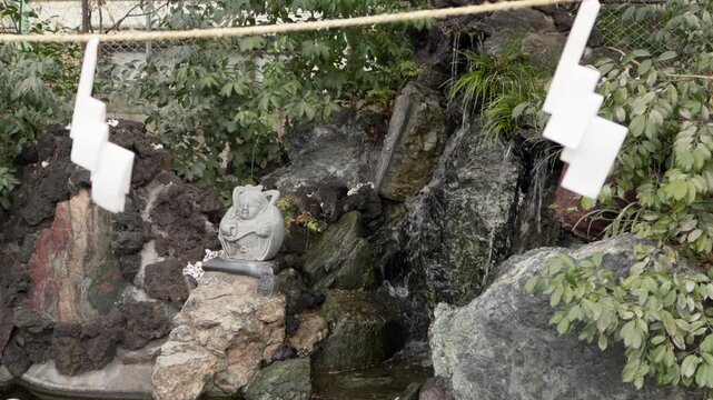 Stone Buddha fountain with flowing water and shide charms at Kawagoe Kumano Shrine a historic Japanese temple known for good fortune and health