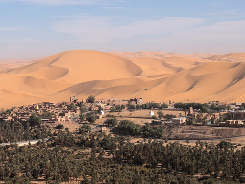 Aerial panoramic view of Taghit oasis town surrounded by massive Sahara sand dunes and palm grove, Algeria
