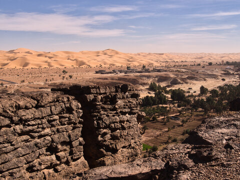 Ancient mud brick ruins overlooking desert oasis valley with palm gardens and vast Sahara sand dunes, Taghit, Algeria