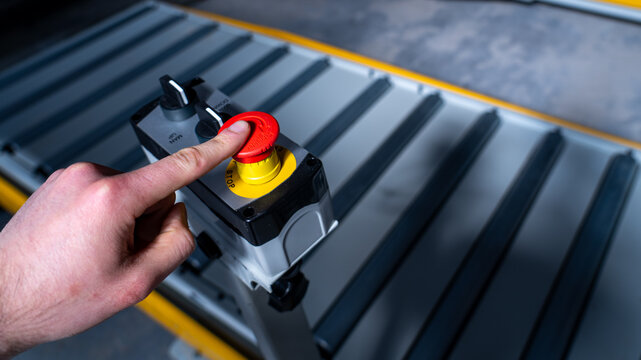 Close-up of worker pressing emergency stop button on industrial machinery.