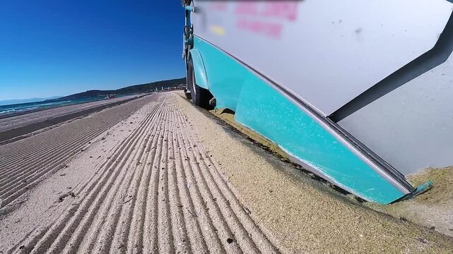 Beach Cleaning Machine Leveling Sand on Pristine Shore, Tractor Grooming Tourist Resort Beach, Low Angle Wide Shot. Sunny day at a coastal destination, preparing the beach for tourists.