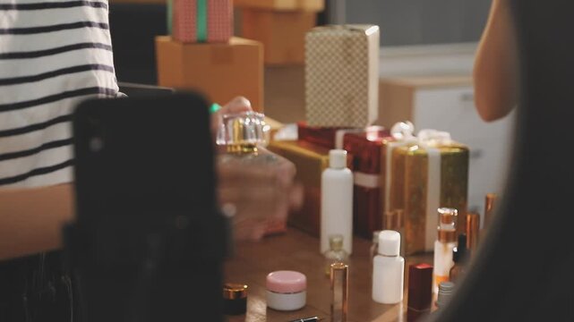 Young beautiful Asian girl reviewing cosmetic and skin care product with new collection's promotion selling on social media online live blurred phone screen surrounded beauty merchandise. Stratagem.