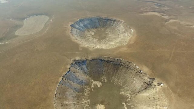 Aerial meteor craters across barren flat plain with dramatic impact geology under clear sky. Desolate treeless landscape reveals circular scars and vast empty terrain expansive wilderness grandeur.