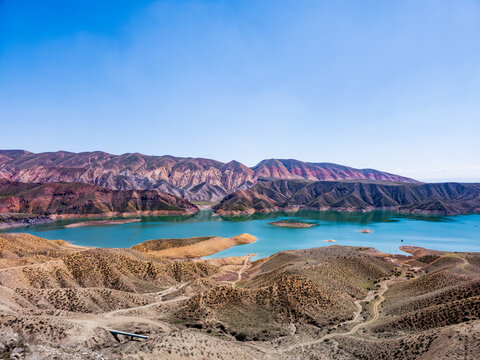 Blue sky above a calm turquoise lake surrounded by red-brown mountain ridges