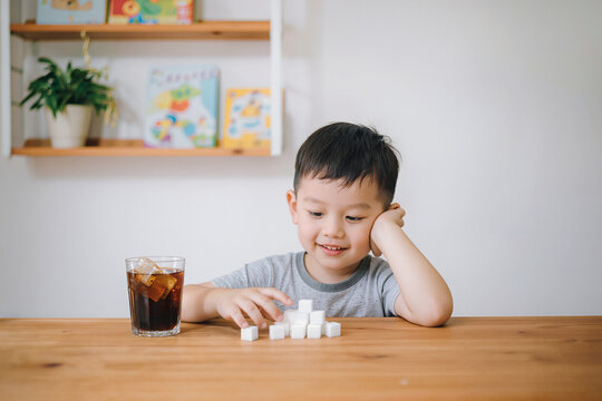 Child examining sugar cubes beside cola drink while sitting thoughtfully at white table indoors.