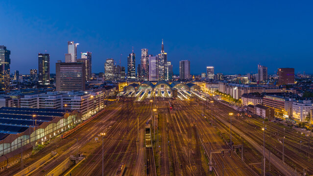 Aerial view of the Hauptbahnhof train station and illuminated railway tracks with the city skyline in the background at twilight in Frankfurt am Main, Hessen, Germany.