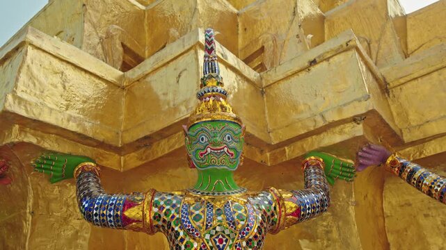 Green guardian demon statue supporting golden chedi at Wat Phra Kaew in Bangkok, traditional Thai temple art in Thailand