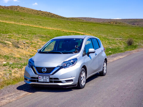 Compact car travels along asphalt road surrounded by hills
