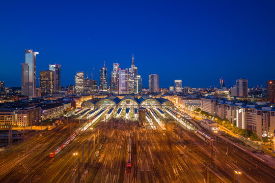 Aerial view of Hauptbahnhof central station with illuminated tracks and the modern city skyline at twilight in Frankfurt am Main, Hessen, Germany.