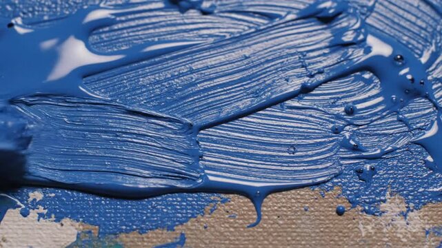 Close up view of paintbrush spreading vibrant blue oil paint on canvas creating texture and artistic brushstrokes
