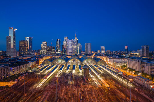 Aerial view of Hauptbahnhof with illuminated train platforms and the city skyline under a twilight sky in Frankfurt am Main, Hessen, Germany.