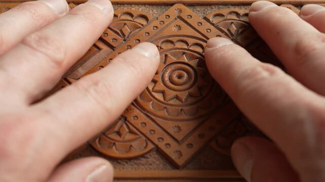 Close up of male fingers touching detailed carved wooden ornament on a jewelry box. Concept of craftsmanship, handmade art, tradition and tactile texture.
