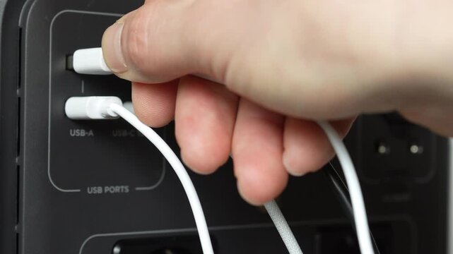 Close up of man hand plugging white USB cable into portable power station. Charging process, connecting device to power source, modern energy and electronics concept.
