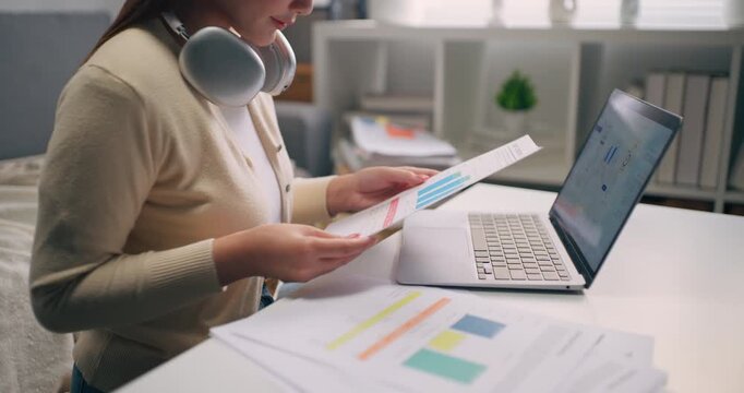 Close-up side view of female hand typing on laptop keyboard with business report and graph on table. financial analysis, data research, and remote work at home.