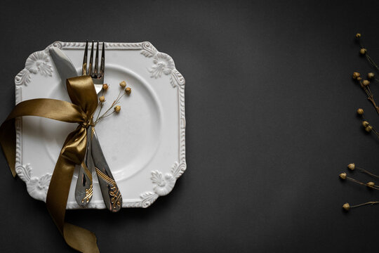 Romantic tabble setting with ribbon, plates, cutlery on black background. Empty plate. Mockup design layout for your text. Love romantic concept. Copy space. Top view. Flat lay.