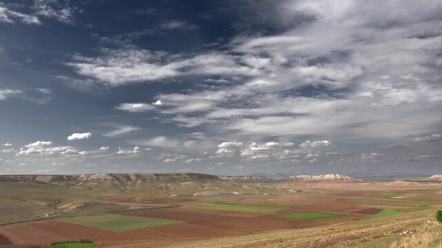 Timelapse USA farmland beneath partly cloudy sky patchwork fields across arid valley. Fast cumulus drift above cropland basin treeless parcels broad american plains rural terrain detail.